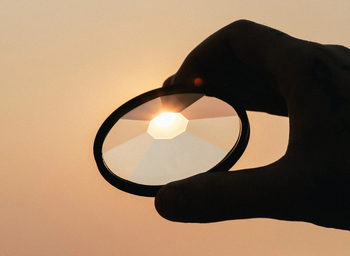 Someone holding a magnifying glass filter and looking through it at the sun