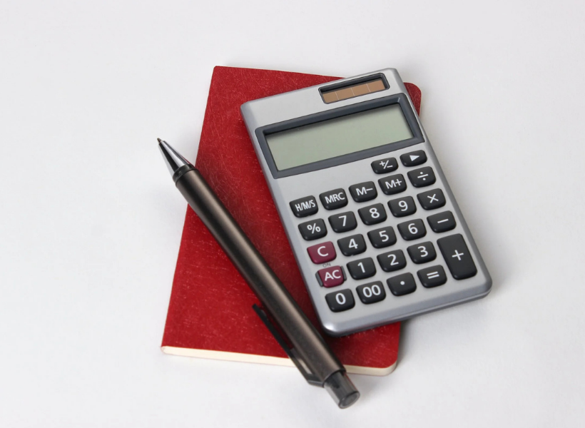 A calculator laying over a red notebook next to a pen