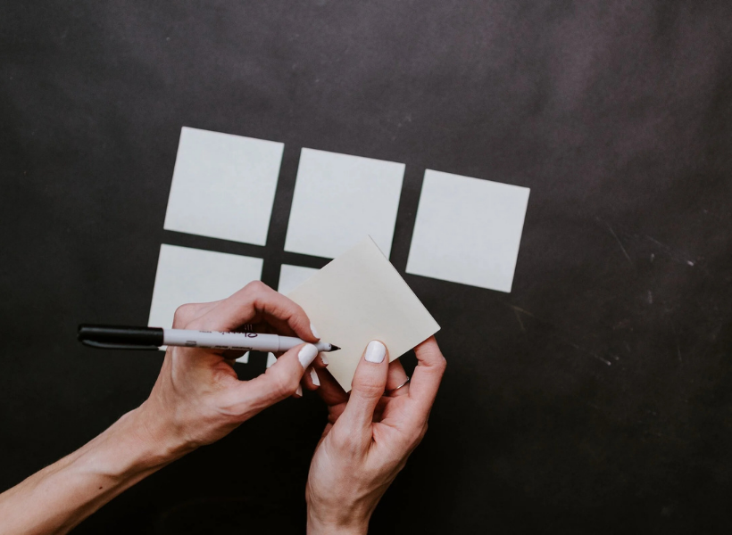 An image of a person writing on a sticky note while 5 other sticky notes lay in the background