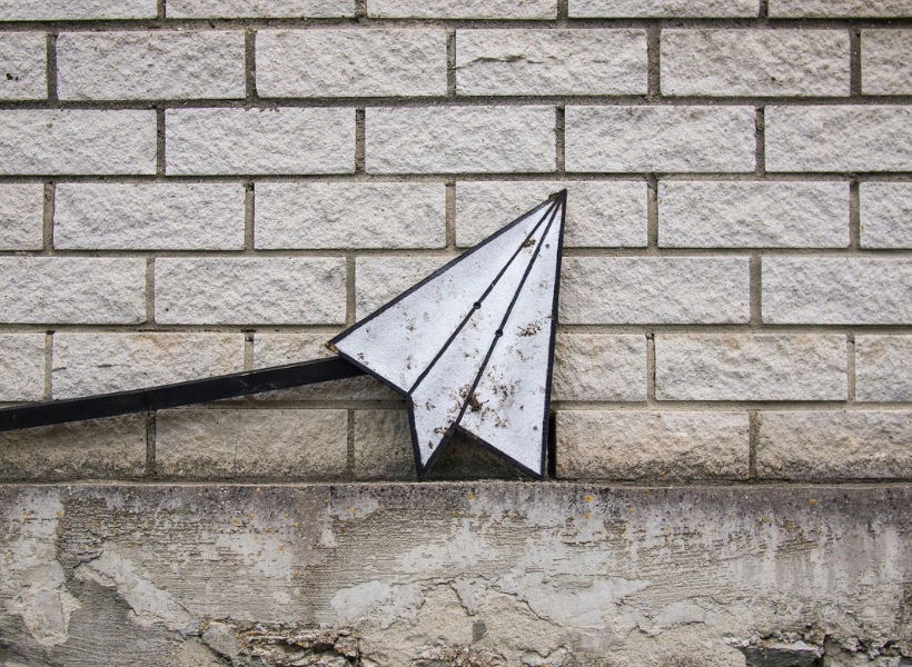 A paper airplane over a gray brick wall